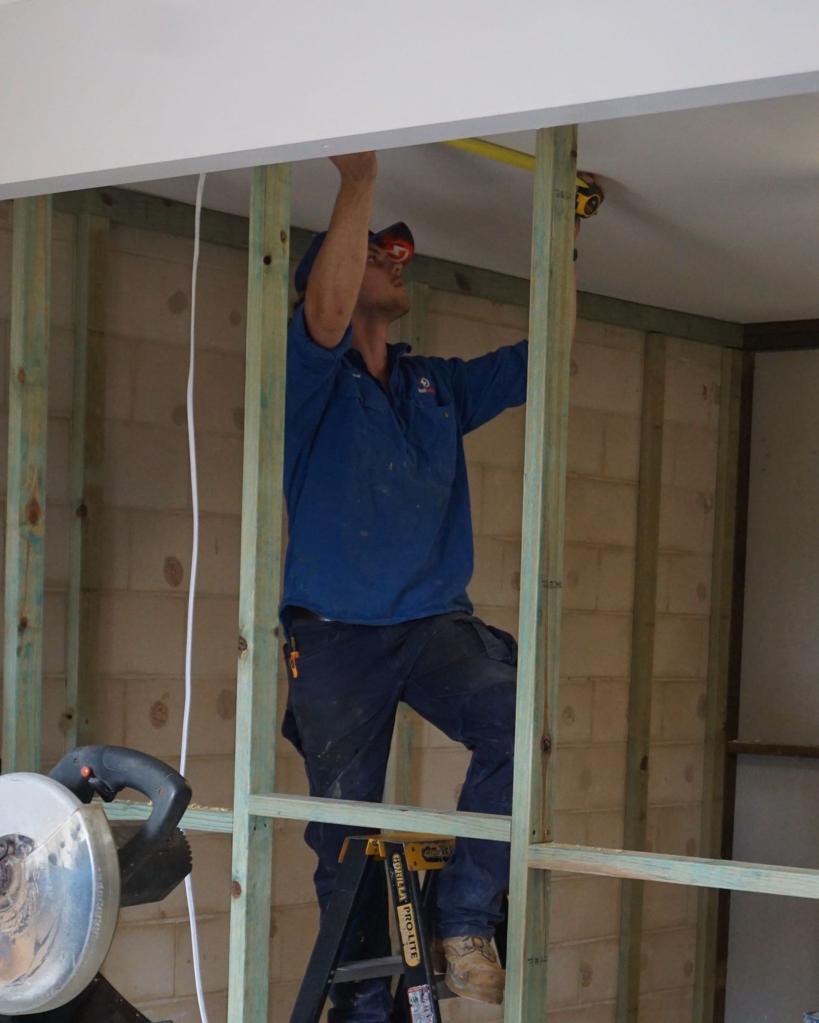 An electrician on a ladder running cable through new ceiling framing during a home renovation