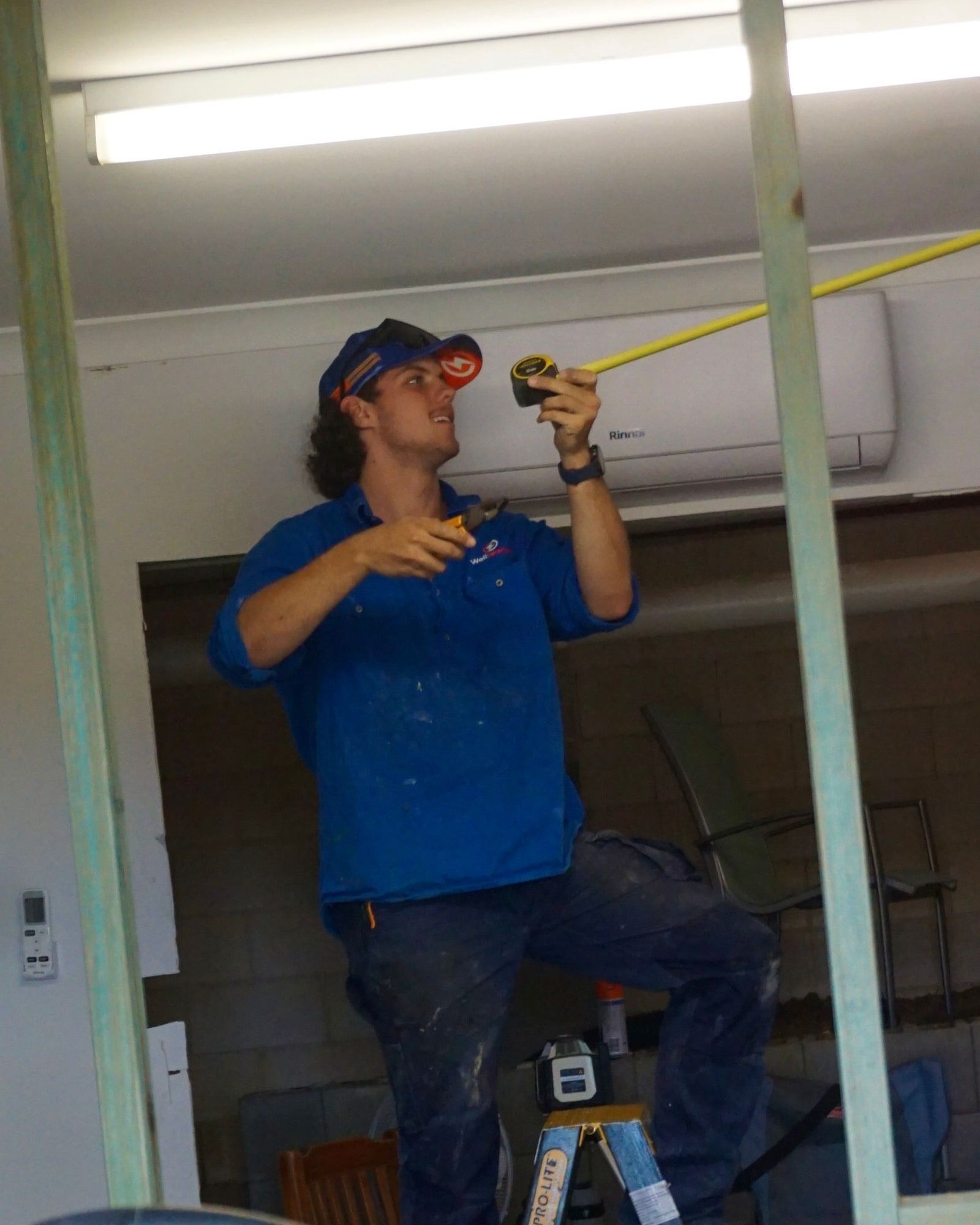 An electrician on a ladder measuring up before fitting off lights in a garage