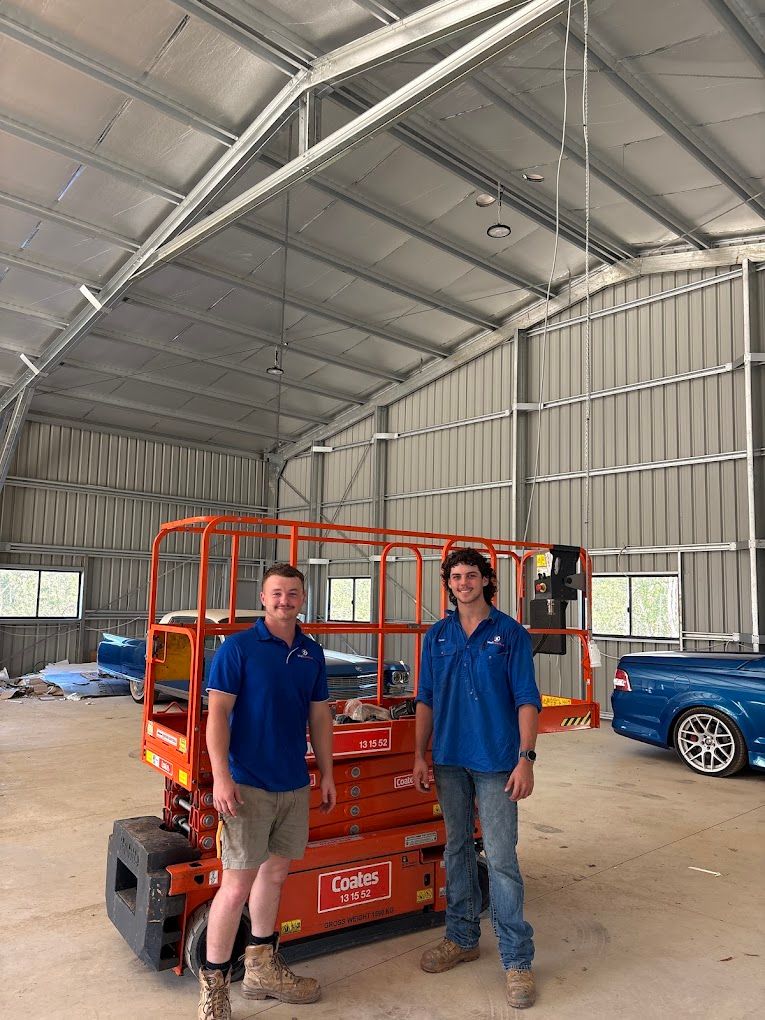 Rory and Oscar beside a scissor lift inside a large steel shed