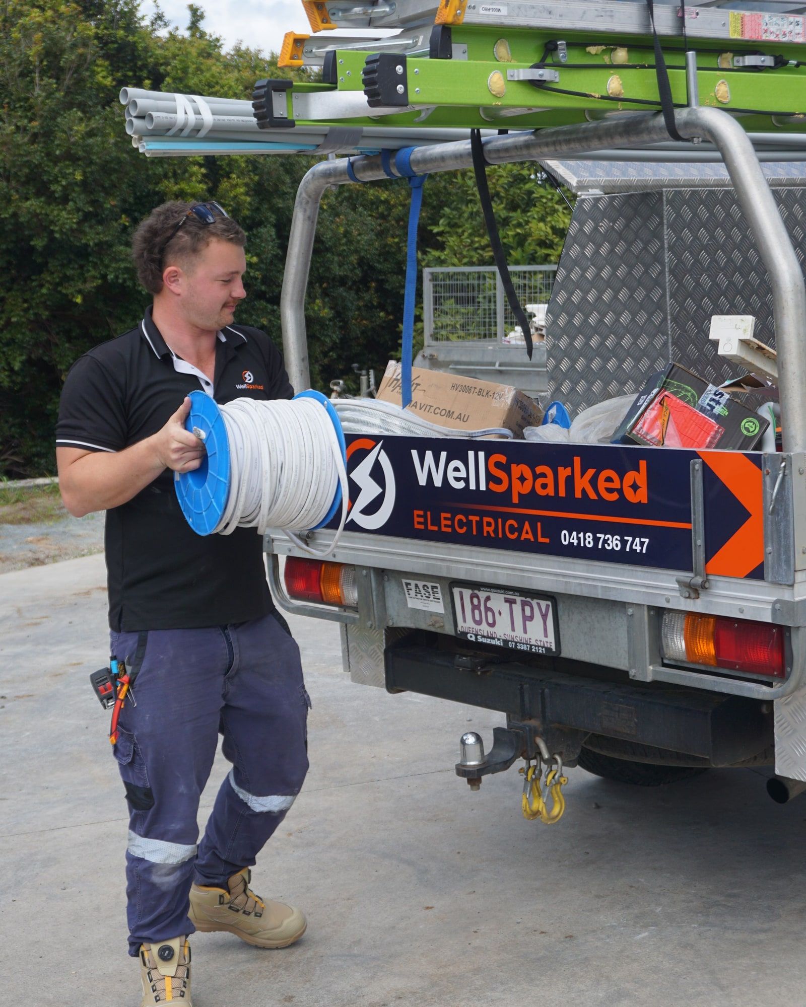 An electrician carrying a reel of cable past the back of the Well Sparked work ute
