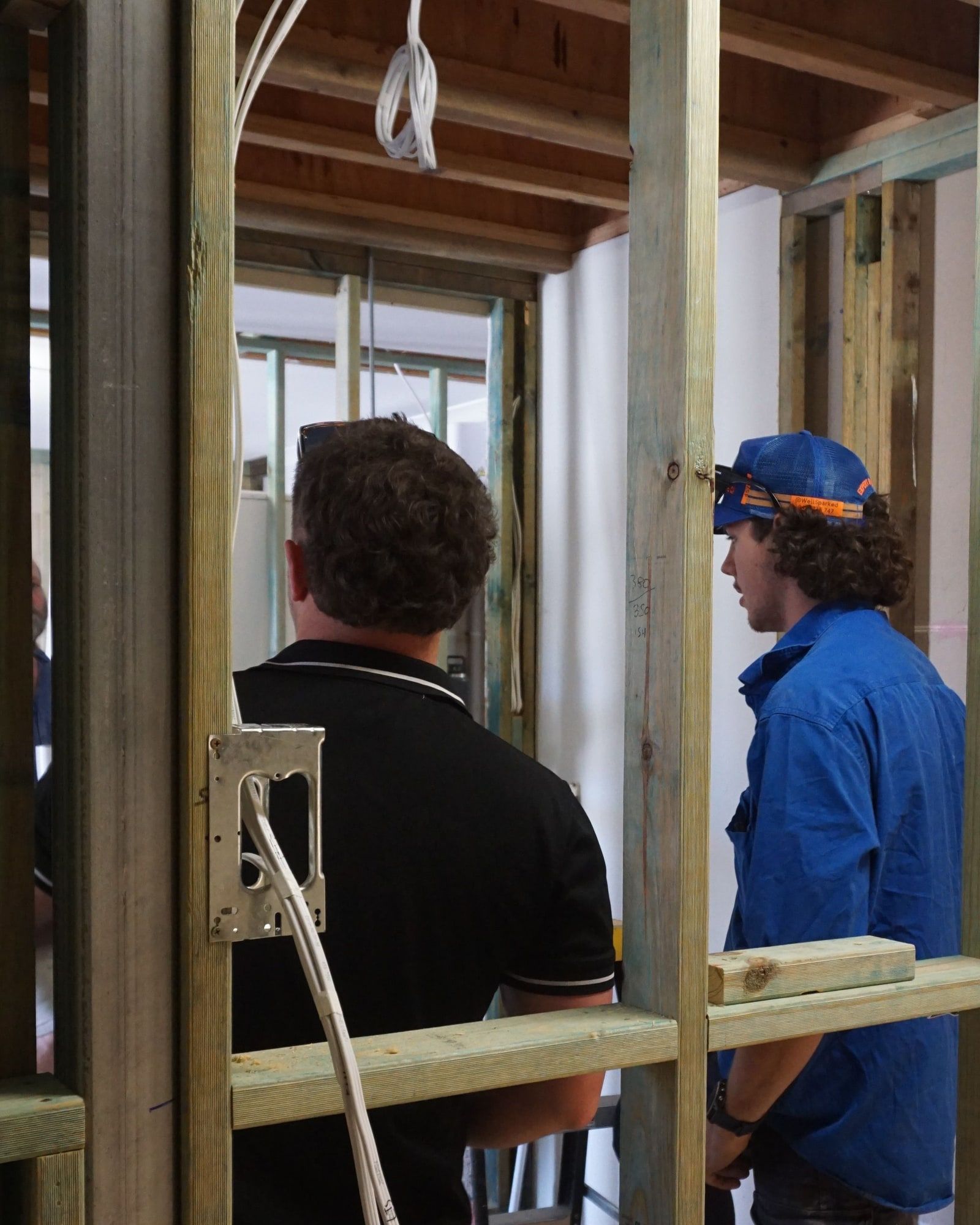 Two electricians wiring a stud wall, with cable run down to a new power point bracket